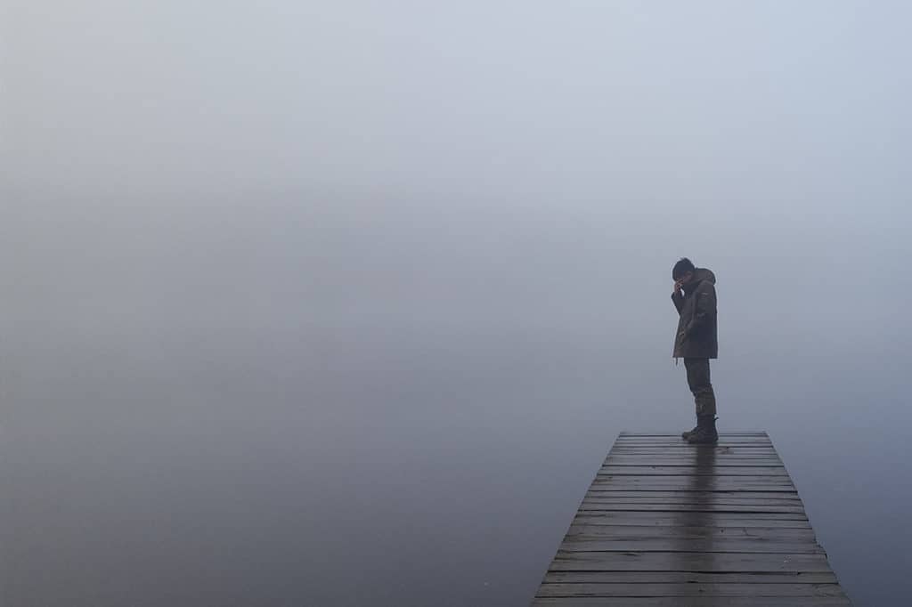 man showing signs of ptsd standing on a dock on a foggy lake