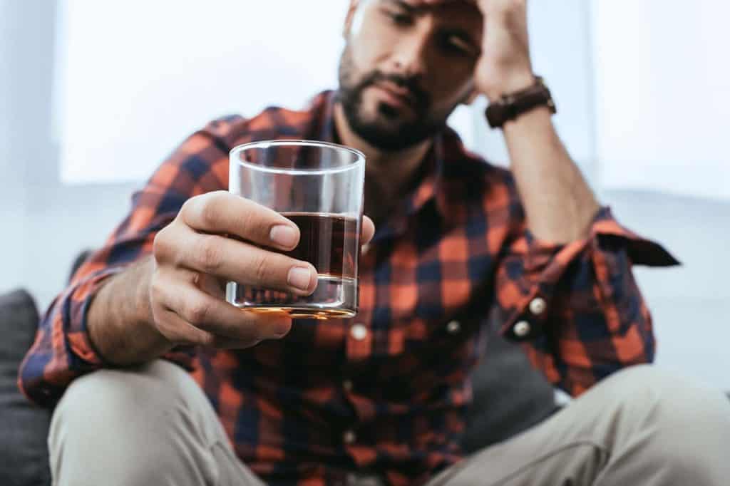 man sitting on couch struggling with alcoholism