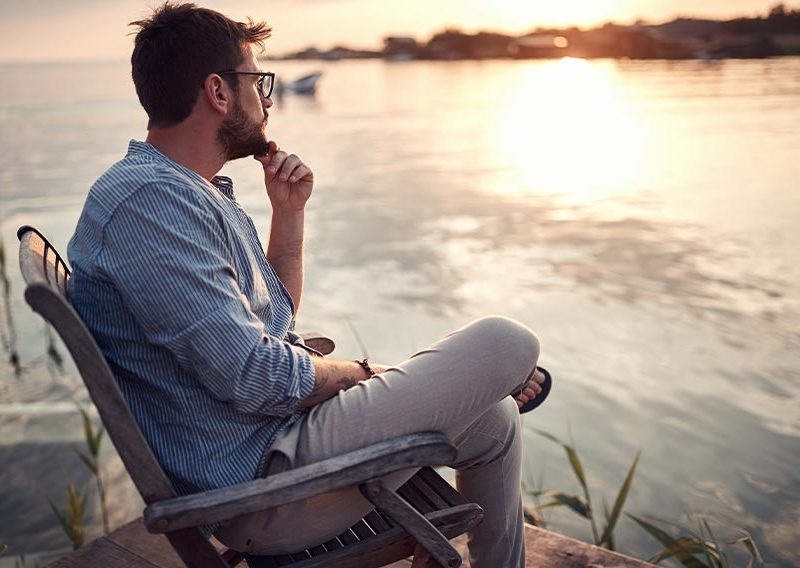 man sitting in a chair by a lake thinking after a relapse