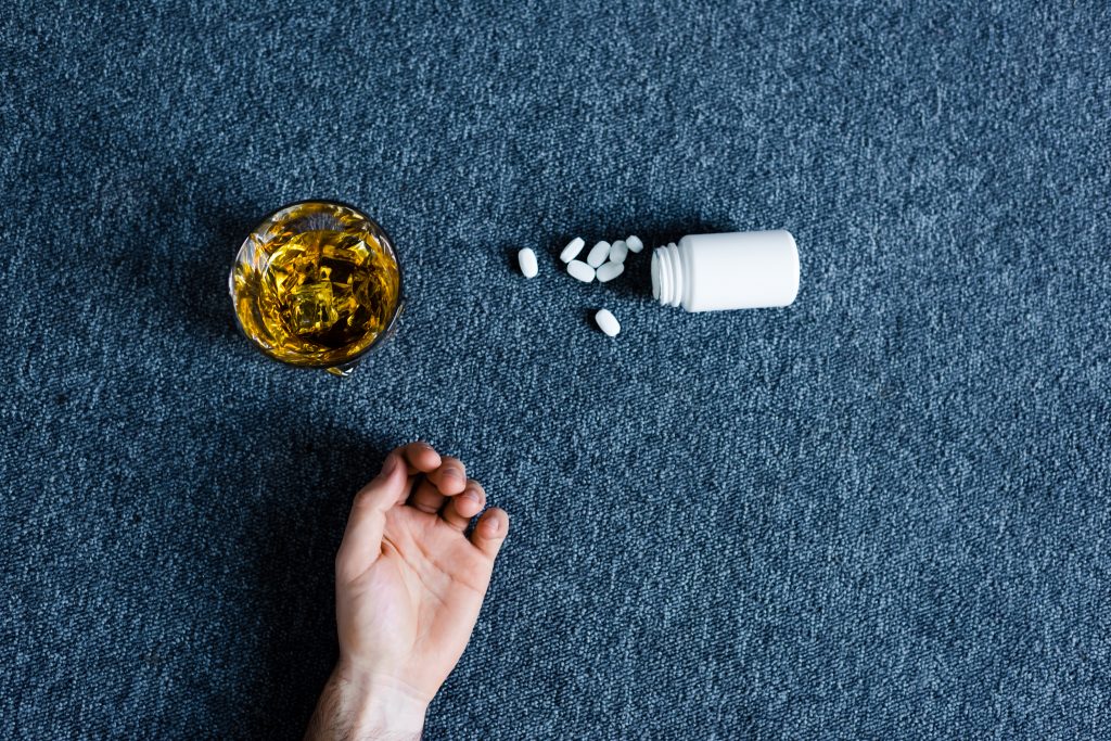 top view of male hand near container with pills near glass of whiskey and container with pills